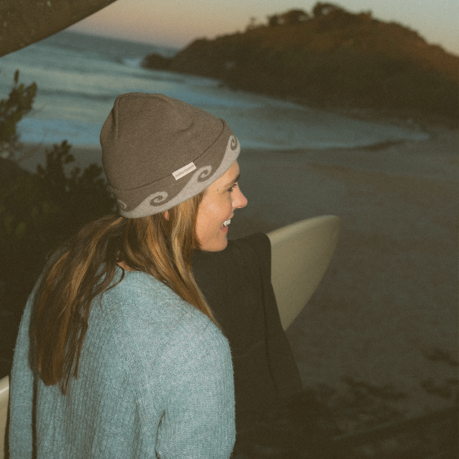 Person wearing a merino wool beanie and sweater on a beach with a sunset in the background
