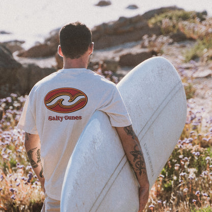 Man with surfboard wearing australian made classics tidal t-shirt while walking down to the beach