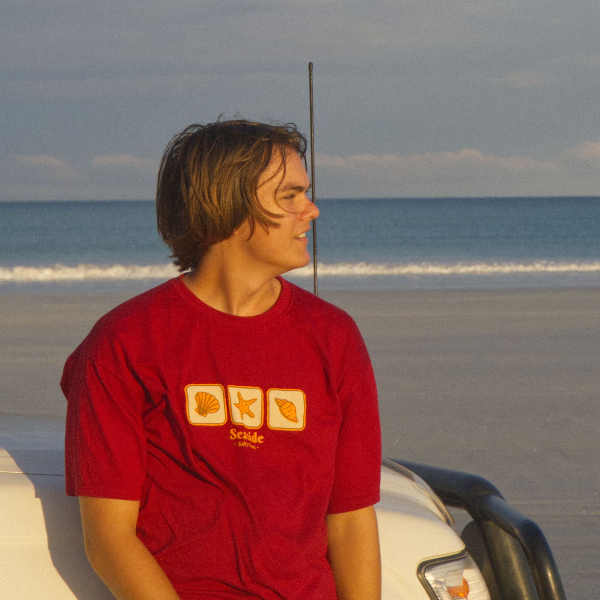 Man wearing Australian made seaside tee at beach leaning on car