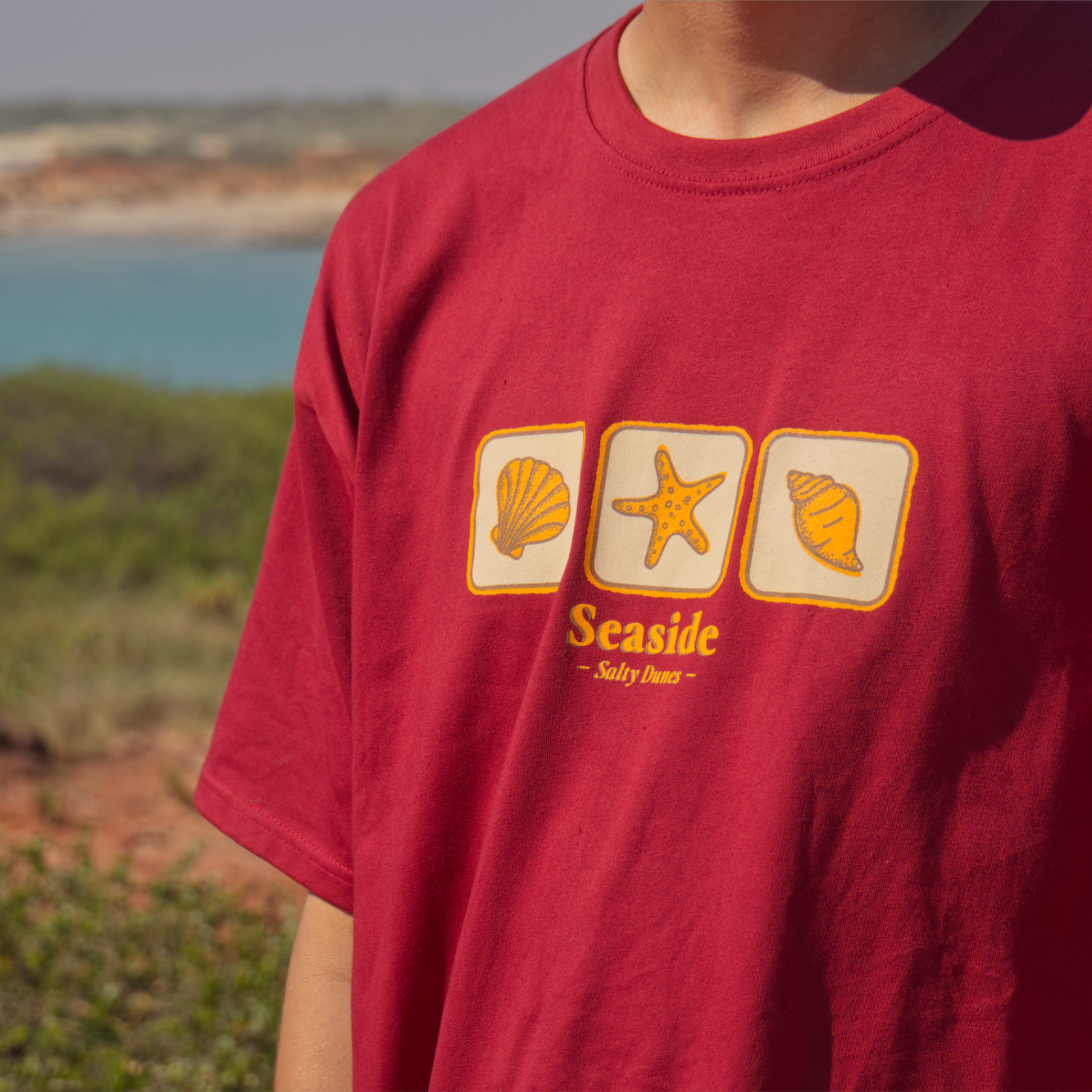 Red seaside tshirt with seashells and starfish.Vintage styled with beach in background and Australian Made