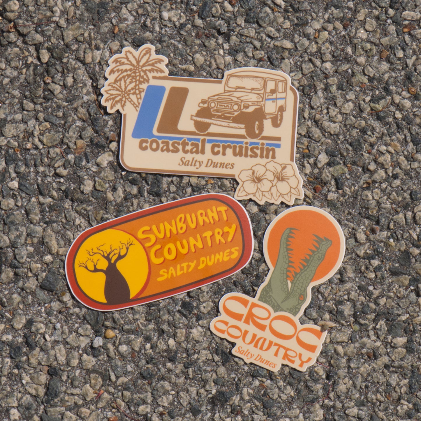 Three stickers with 'Salty Dunes' branding on bitumen surface