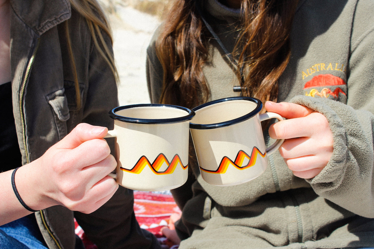 Two people each holding a Classics Enamel Camp Mug and making them cheers