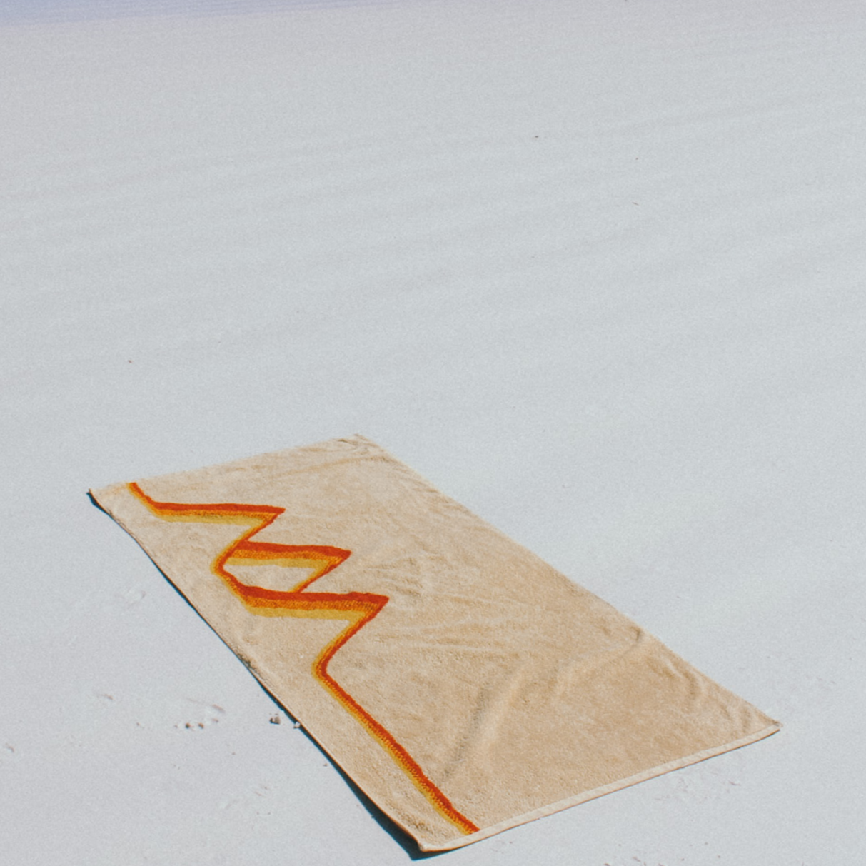 The Classics Beach Towel is laying down on a white, sandy beach.