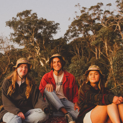 Group of three on a rock each wearing the classics hemp wide brim hat in olive green