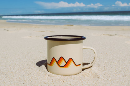 The Classics Enamel Camp mug sitting in the sand on the beach