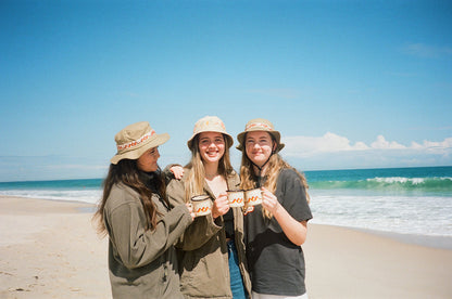 Three girls on the beach holding Salty Dunes Enamel Camp mugs with the ocean in the background